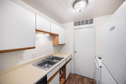 A small kitchen with white cabinets and a white fridge.
