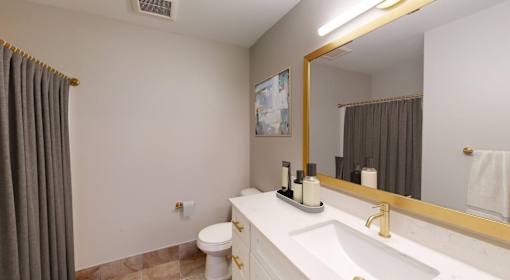 A bathroom with a white counter and a gold framed mirror.