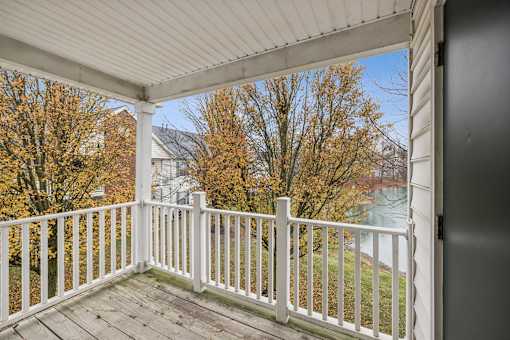 A white porch with a view of a tree with orange leaves.
