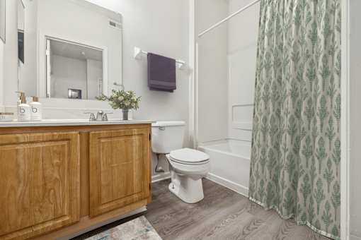 A bathroom with a wooden vanity, white toilet, and a green shower curtain.