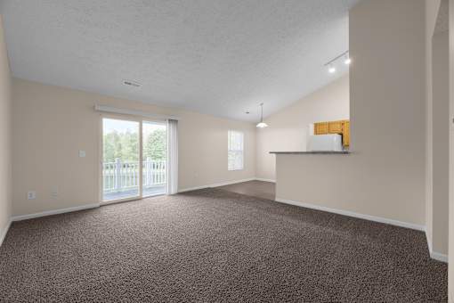 A large, empty room with carpeted floor and a sliding glass door leading to a deck.