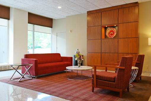 A red couch sits in a room with a wooden panel wall and a painting on it.