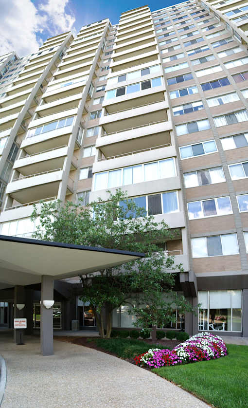 A tall building with a lot of windows and a small garden in front.