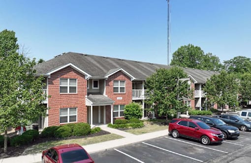 A red car is parked in a parking lot in front of a brick building.