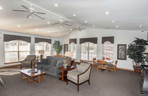 A living room with a grey couch, wooden chairs, and a ceiling fan.
