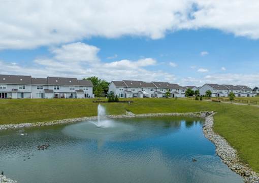 A fountain in the middle of a pond in front of a row of houses.