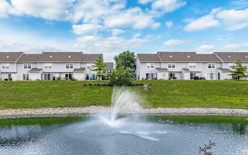 A fountain in the middle of a pond with houses in the background.
