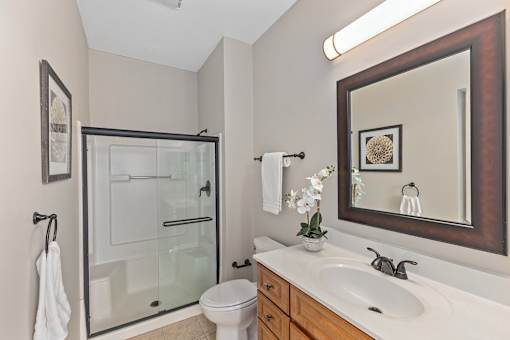 A bathroom with a toilet, sink, mirror and shower.