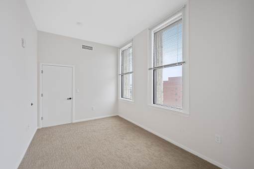 A room with a white door, carpeted floor, and a window with blinds at Sky Central Apartments, Cincinnati, 45202