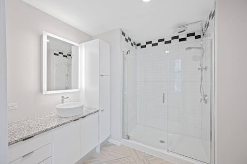A white bathroom with a sink, mirror, and shower at Sky Central Apartments, Cincinnati, Ohio