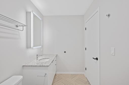 A white bathroom with a toilet, sink, and mirror at Sky Central Apartments, Ohio