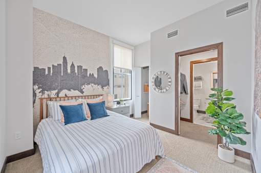 A bedroom with a bed, a plant, and a city skyline mural on the wall at Sky Central Apartments, Cincinnati