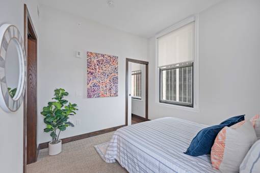 A bedroom with a bed, a plant, and a painting on the wall at Sky Central Apartments, Cincinnati, OH, 45202