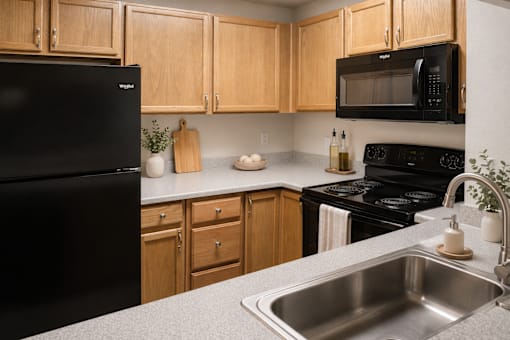 A kitchen with a black refrigerator, wooden cabinets, and a black microwave.