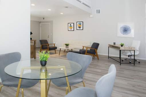 A glass table with grey chairs in a room with white walls.