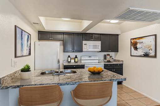 A kitchen with a white refrigerator, black cabinets, and a marble countertop.