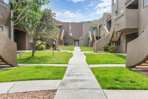 A concrete pathway leads through a grassy area between two rows of concrete buildings.