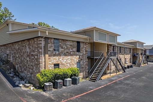 A parking lot in front of a building with a stone wall and a metal staircase.