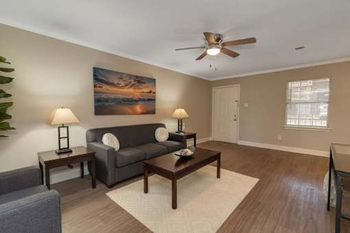 A living room with a grey couch, a painting on the wall, and a ceiling fan.