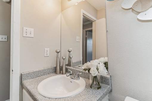 A bathroom with a sink, mirror, and flowers.