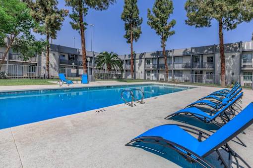 A pool with blue chairs and trees in front of a building.