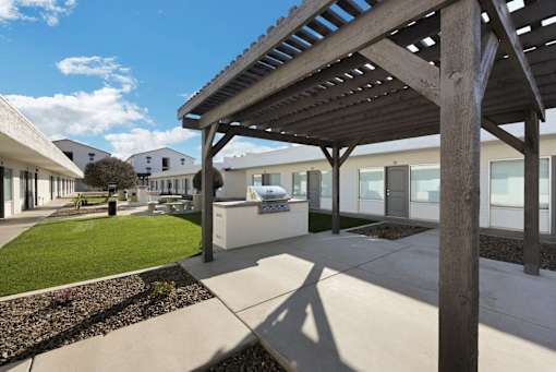 A wooden pergola is over a patio with a concrete floor.