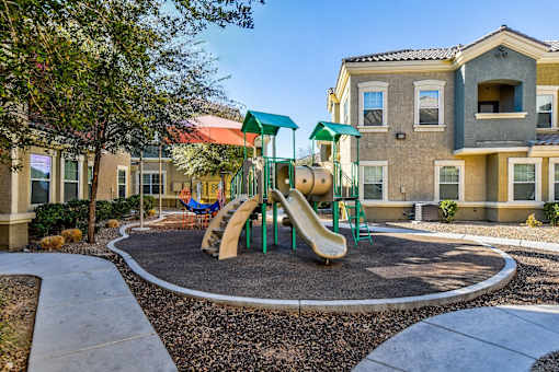 A playground with a green slide and a yellow slide in front of a building.
