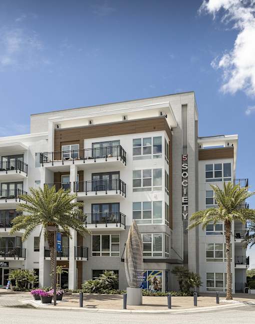 A modern apartment building named "Society" with balconies and palm trees in front.