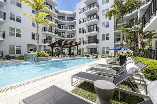 A pool area with sun loungers and a building in the background.
