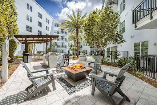 A patio with chairs and a fire pit in front of a white building.