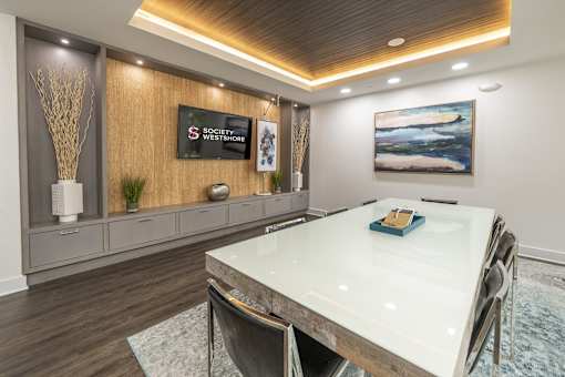 A conference room with a long table and chairs, a TV screen displaying "Social Westmore" and a painting on the wall.