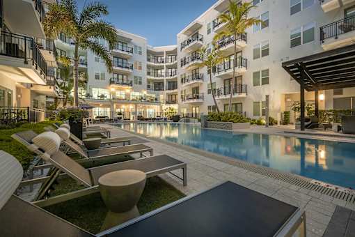 A modern apartment complex with a pool and lounge chairs.
