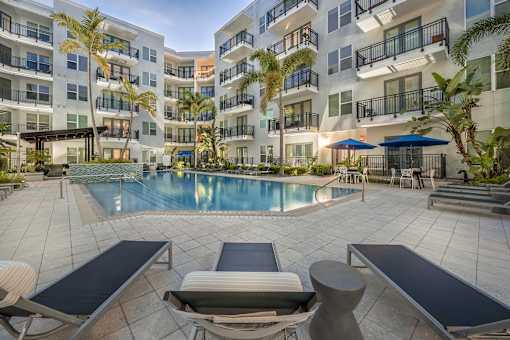 A pool surrounded by lounge chairs and umbrellas in front of a building.