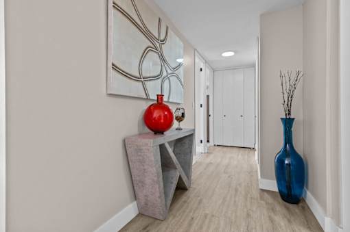A hallway with a red vase on a table and a blue vase on the floor.
