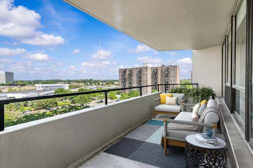 A balcony with a couch, chairs, and a table overlooking a cityscape.
