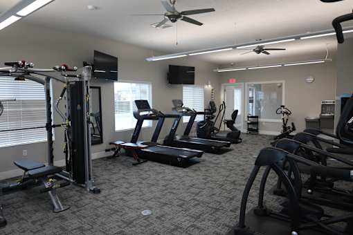 A gym with a variety of equipment including treadmills, weights, and a television.