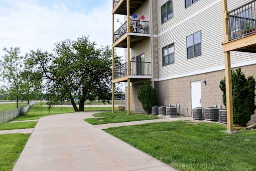 A concrete walkway leads to a building with a balcony.