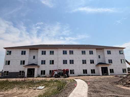 A large white building under construction with a red vehicle in front.
