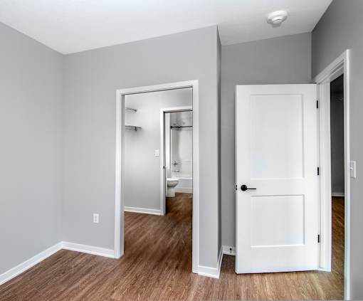 an empty room with a white door and a hallway to a bathroom