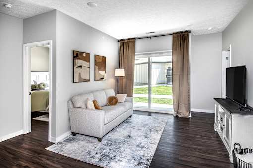 A living room with a grey couch, a television, and a large window with curtains.