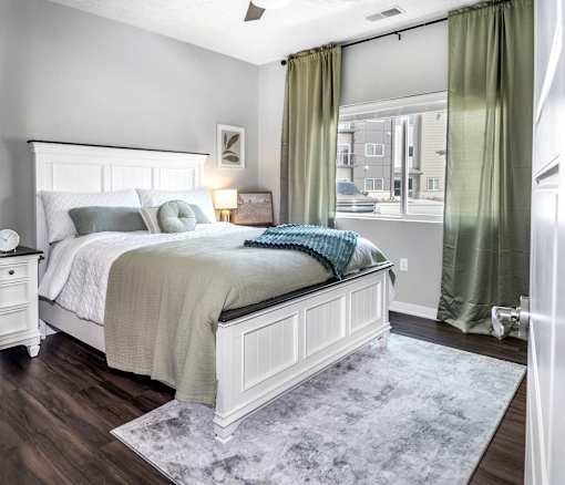 A bedroom with a large bed and a window with green curtains.