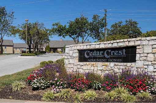 The Cedar Crest Apartments sign displayed in front of a stone wall, surrounded by flowers and landscaping.