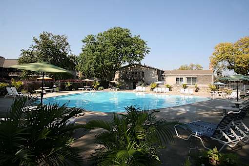 A swimming pool with chairs and a building in the background at Eden West Apartments.
