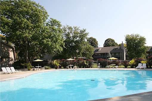 A swimming pool with trees and a house in the background at Eden West Apartments.