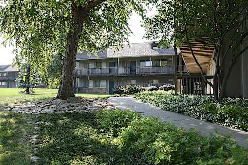 A building at Eden West Apartments with a tree and a sidewalk in front of it.