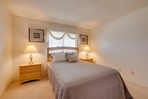 Bedroom in the one-bedroom model unit at Olde English Village, featuring a comfortable bed and natural light.