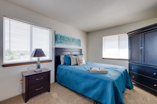 Bright bedroom in the two-bedroom model unit at Olde English Village, showcasing a large window and well-appointed furnishings.