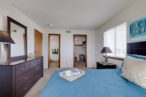 Bright bedroom in the two-bedroom model unit at Olde English Village, showcasing a large window and well-appointed furnishings.