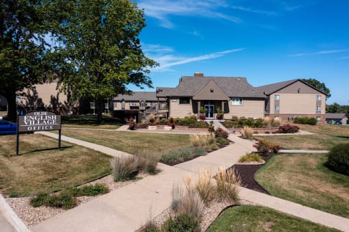 The Olde English Village clubhouse exterior is surrounded by well-maintained landscaping, creating a welcoming central gathering space for residents.