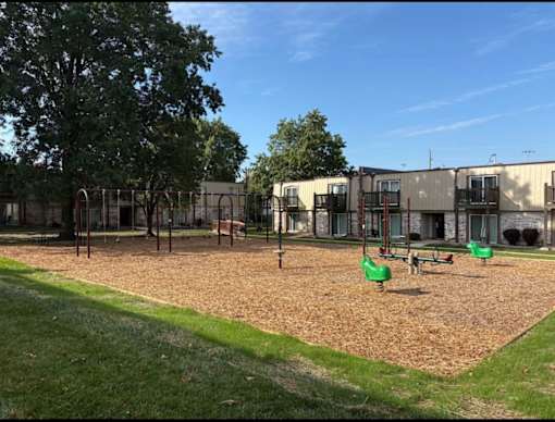 Playground with green swing set and sandbox at Park 25 Apartments surrounded by open outdoor space.